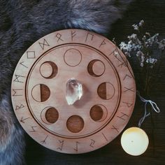 a wooden plate with the moon phases on it next to a candle and some flowers