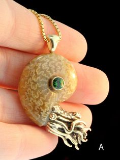 "This remarkable Nautilus Pendant features an ammonite fossil bezel set with a 5mm gemstone. These are the first of Alisha's Nautilus' to be cast in 14k Gold. Alisha hand picks each fossilized ammonite and finding specimens of this quality is rare. These pendants measure approximately 2\" diagonally from the bail to the tip of the tentacles. They are drilled and pegged securely into especially beautiful miniature fossilized ammonite shells. The fossilized shells shimmer subtly with iridescence a Luxury Untreated Jewelry For Gift, Luxury Untreated Jewelry As A Gift, Unique Spiral Yellow Gold Jewelry, Unique Yellow Gold Spiral Jewelry, Unique Gold-colored Sterling Silver Gemstones, Unique Yellow Gold Sterling Silver Gemstones, Luxury Spiral-shaped Jewelry Gift, Luxury Spiral Jewelry Gift, Luxury Spiral Jewelry As A Gift