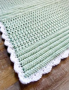 a green and white crocheted blanket sitting on top of a wooden floor