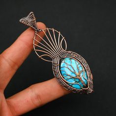 a hand holding a wire wrapped pendant with a turquoise stone in the center and tree on it