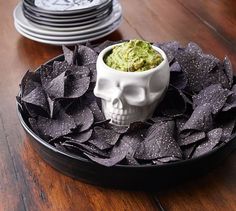 a plate with chips and guacamole in it on a wooden table next to stacks of plates