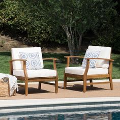 two chairs sitting next to each other near a swimming pool with trees in the background