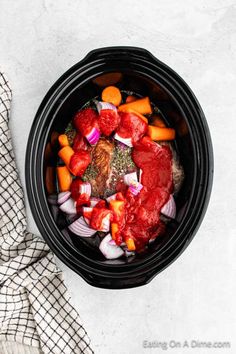 a slow cooker filled with meat, vegetables and sauce on a towel next to a cloth