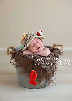 a baby is laying in a bucket wearing a hat and holding a red ornament