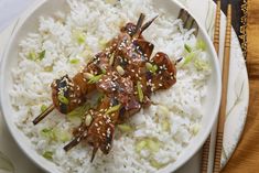 a white plate topped with rice and meat covered in sesame seed sauce next to chopsticks