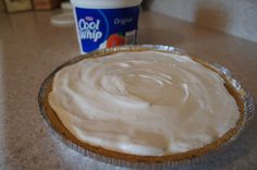 a pie with frosting sitting on top of a counter next to a cup of yogurt