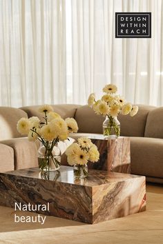 two vases with flowers sit on a table in front of a couch