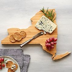 a wooden cutting board topped with crackers and grapes next to a plate of cheese