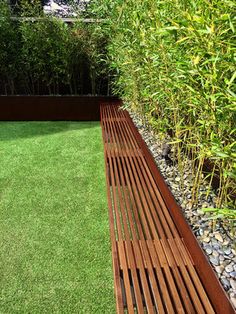 a wooden bench sitting on top of a lush green grass covered field next to a bush