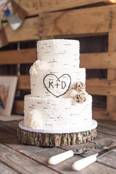 a wedding cake with initials on it sitting on a table next to some forks and spoons