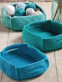 two knitted baskets sitting on top of a wooden floor next to vases filled with balls of yarn