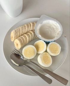 a plate with sliced bananas, hard boiled eggs and yogurt on it next to a fork