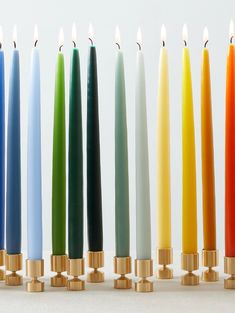 many different colored candles lined up next to each other on a white surface with one candle in the middle