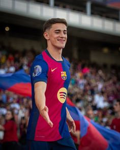 a young man in a blue and pink soccer uniform is walking with his hand out towards the crowd