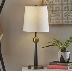 a lamp sitting on top of a white table next to a potted plant and books