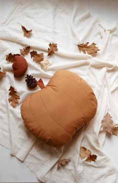 a heart shaped pillow sitting on top of a white blanket covered in leaves and acorns