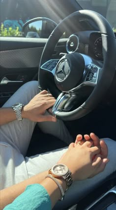 two people holding hands while sitting in the driver's seat of a mercedes car