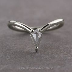 a white gold ring with a triangle shaped diamond on it's side, sitting on a gray surface