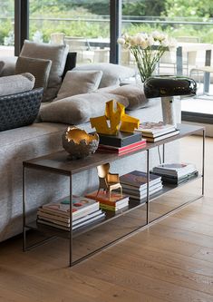 a living room with a couch, coffee table and vases on the tables in front of large windows