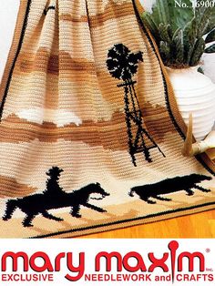 a crocheted blanket with horses and palm trees on it, next to a potted plant