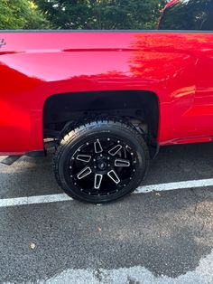 a red truck with black wheels parked in a parking lot next to trees and bushes