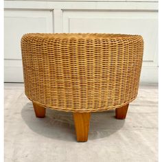 a round wicker ottoman with wooden legs on the floor in front of a white door