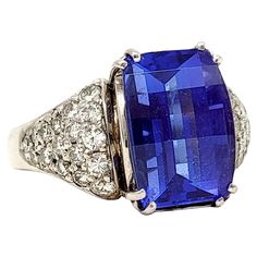 Ring size: 10 Absolutely magnificent tanzanite and diamond ring. The brilliant blue stone against the bright white diamonds really catches the viewers eye while the sizeable stone fills the finger with sparkle. The impressive 7.50 carat prong set rectangular dome step cut tanzanite stone sits at the very center of the piece, demanding the viewers attention. It is a gorgeous, transparent violetish-blue color. Flanking the main stone are 2 triangular shaped clusters of pave diamonds totaling 1.20 Luxury Tanzanite Diamond Ring With Emerald Cut, Formal Tanzanite Diamond Ring With Diamond Accents, Formal Tanzanite Diamond Ring With Accents, Formal Blue Tanzanite Gemstones, Rectangular Blue Diamond Ring, Classic Tanzanite Diamond Ring With Accents, Brilliant Cut Tanzanite Gemstones, Blue Rectangular Diamond Ring For Formal Occasions, Tanzanite And Diamond Ring