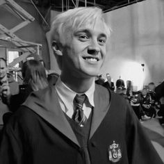 a man with white hair wearing a harry potter outfit and smiling at the camera while standing in front of a group of people