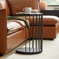 a coffee table with a cup on it next to a brown leather couch and chair