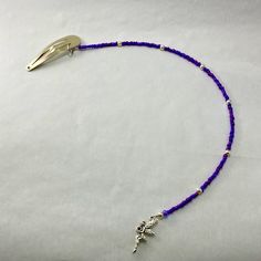 a purple beaded necklace with silver beads and a cross on the end is laying on a white surface