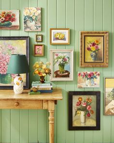 a room with green walls and pictures on the wall next to a wooden table topped with a lamp