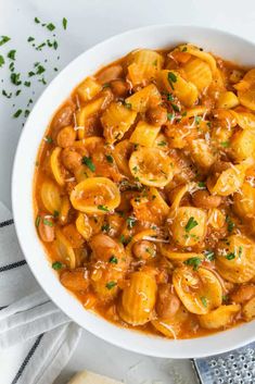 a white bowl filled with pasta and meat in tomato sauce on top of a table