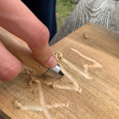 a person is writing on a piece of wood with a small metal object in their hand