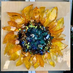 a sunflower made out of glass sitting on top of a piece of plywood