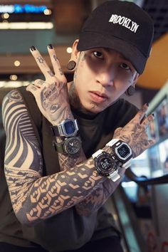 a man with tattoos holding his hand up to the camera while wearing a black hat