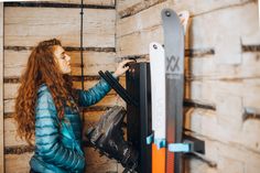 a woman is looking at her skis on the rack in front of a wooden wall