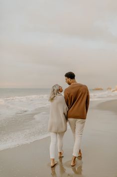 an older couple walking along the beach holding hands and looking at the ocean in front of them