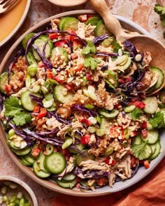 a salad with cucumbers, red cabbage, and chicken in a bowl on a table