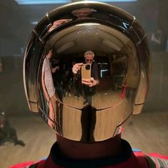 a man taking a selfie with his cell phone in front of a shiny helmet