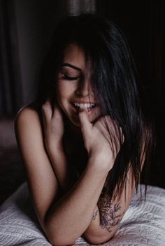 a woman laying on top of a bed with her hand under her chin and smiling