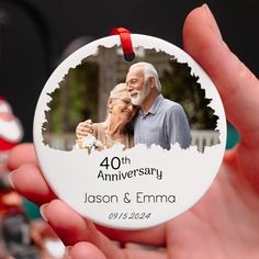 a hand holding a personalized ornament with an image of an elderly man and woman