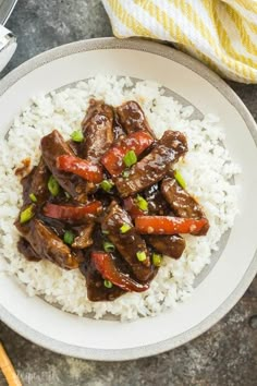 a white plate topped with beef and rice next to chopsticks on a table