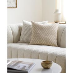 a white couch with pillows on it and a table in front of it, next to a window