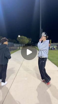 two young men are walking down the sidewalk at night, one is talking on his cell phone