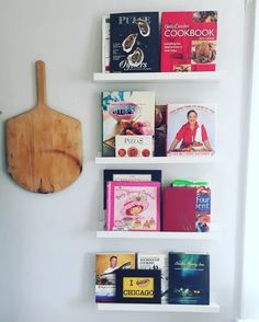 three white shelves with books on them and a cutting board mounted to the wall