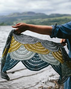 a person holding up a crocheted shawl by the water