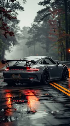 a grey sports car driving down a wet road in the rain with its lights on