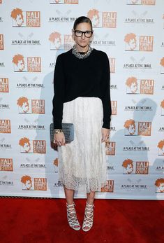 a woman standing on top of a red carpet wearing a white skirt and black sweater