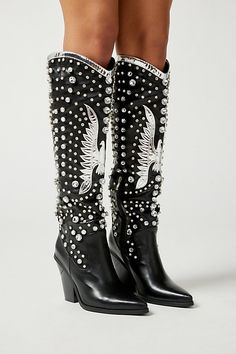 Statement cowboy boots from Azalea Wang in a classic western silhouette topped with tons of rhinestone detailing. Vegan leather in a knee-high length with a metallic patch at the front. Finished with a pointed toe, high heel and hidden zip closure. Features Rhinestone cowboy boots from Azalea Wang Knee-high silhouette in vegan leather High heeled with a pointed toe Zip closure Content + Care Synthetic Wipe clean Imported Size + Fit Shaft: 21" h Heel: 4.25" h | Azalea Wang Upbeat Rhinestone Cowbo Western Rhinestone Fringe Boots For Fall, Western Boots With Rhinestone Fringe For Fall, Western Boots With Rhinestone Rivets For Fall, Western Leather Embellished Boots, Western Style Embellished Leather Boots, Embellished Festival Boots For Fall, Western Style Moto Boots For Winter Party, Western Style Knee-high Boots With Pointed Toe For Party, Western Embellished Snip Toe Boots