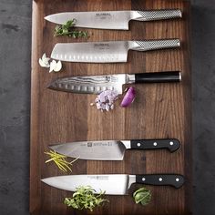 several knives are lined up on a cutting board with flowers and herbs next to them